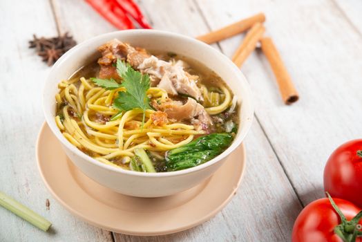 Asian soup noodles and chicken in bowl on wooden background. 