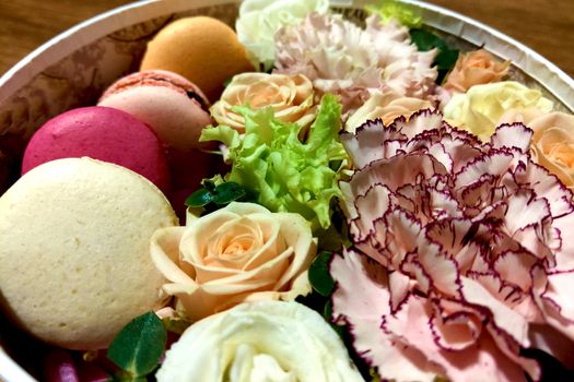 Delicious colourful macaroons cookies in a gift box along with blossoming flower bouquet of roses, mattiola, carnations