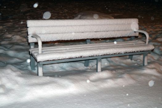 Snow-covered bench in the evening park