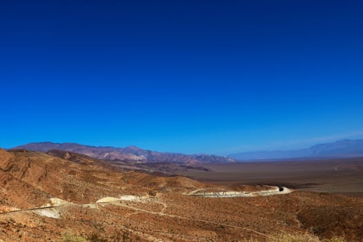 Scanty vegetation and a dirt road winding towards the horizon in the Bolivian altiplano against the background of mountains