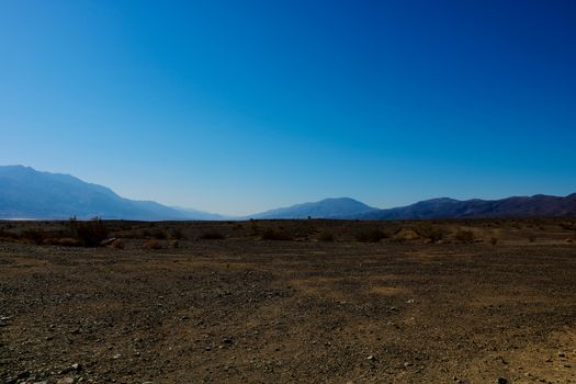 Bright sunny view over Death Valley from Hell's Gate viewpoint in a landscaped of scattered rocks and shrubs - California