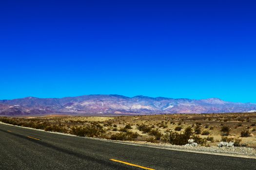 Classic vertical panorama view of an endless straight road running through the barren scenery of the American Southwest with extreme heat haze on a beautiful hot sunny day with blue sky in summer.