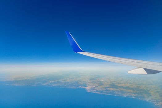 Airplane wing on the sky over sea and land.