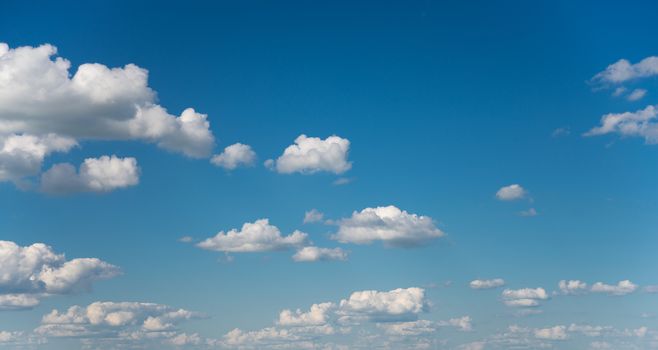 Panorama of vast blue summer sky with fluffy white cumulus clouds