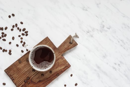 Morning composition with a cup of black coffee and coffee beans on a marble surface with space for text, top view