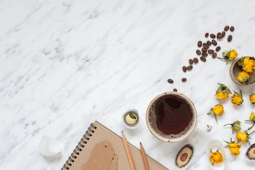 Morning composition with a cup of black coffee, chocolate candies and a notebook on a marble surface with space for text, top view