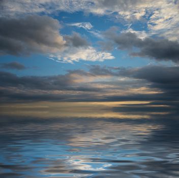 Beautiful seascape with dramatic sunset sky with dark clouds reflected in a water surface with small waves