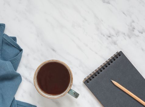 Morning composition with cup of black coffee, blue napkin and notebook on a marble surface, with space for text, top view