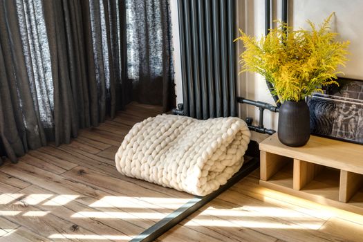 Modern Nordic Scandinavian interior design. A soft knitted plaid on a floor near a vase with the flowers a mimosa.