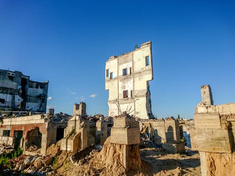 The ruins of a large destroyed building, pieces of stone, concrete, clay and metal against the blue clear sky