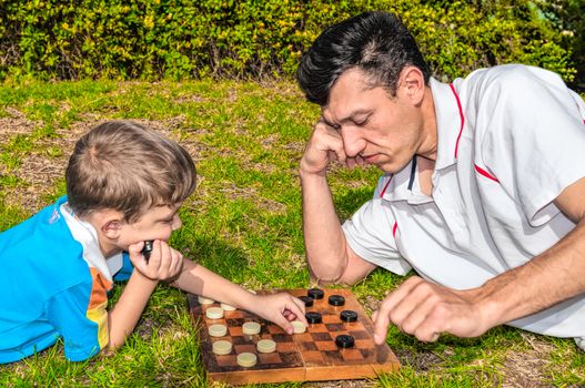 Father and son playing checkers on the grass in a city park