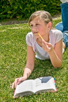 Girl resting with a book on the grass in the park. thought looking to the side