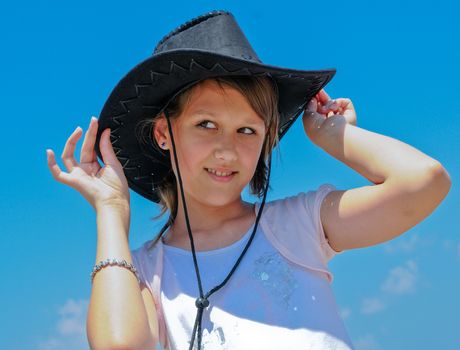 Teenage girl trying on a black cowboy hat against a blue sky
and  looking at her boyfriend
