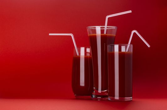 Glass of tomato juice isolated on red background with copy space, bloody Mary cocktail