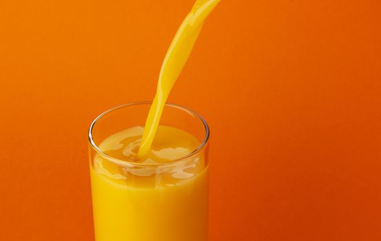 Orange juice pouring into glass, isolated on colour background, with copy space, healthy drink concept, close-up