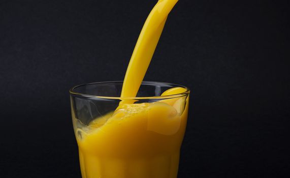 Orange juice pouring into glass, isolated on black background, with copy space, healthy drink concept, close-up