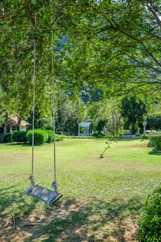 Image of wooden swing under the tree in the garden