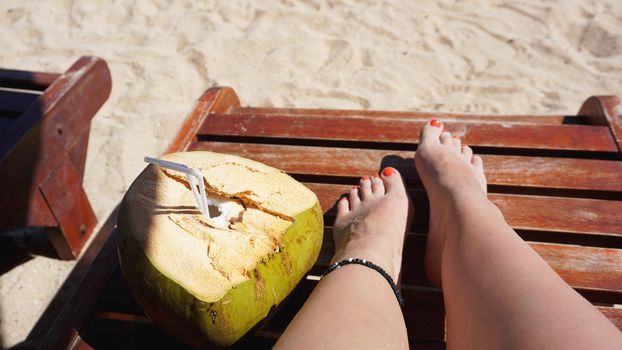 Female legs and coconut drink on the beach, travel and relax
