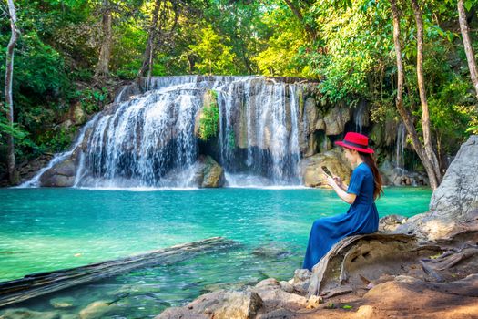 Woman sitting at Erawan waterfall in Thailand. Beautiful waterfall with emerald pool in nature.