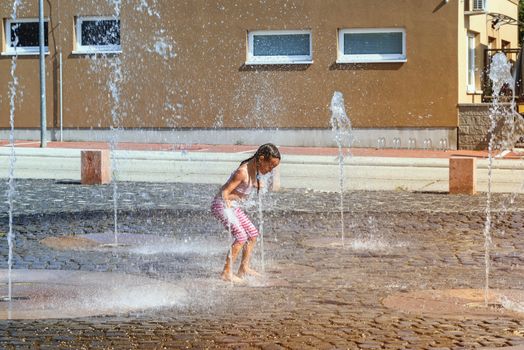 Girl on a sunny summer day are poured water from a fountain.Girl happily in shallow clean water on of city fountain on warm bright summer day.
