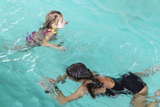 Two sisters in the pool. Two happy girls play in the pool.Beautiful girls swim and having fun in water.Active holiday.Two girls swim in the pool.