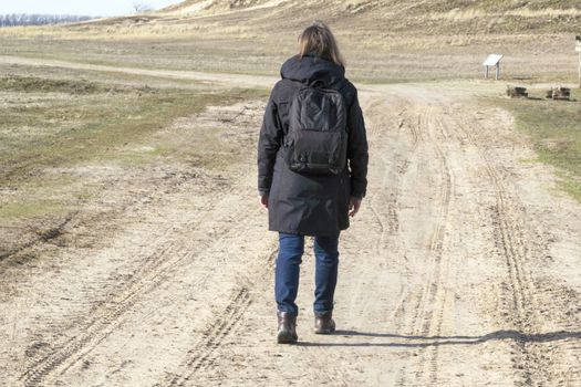 Caucasian woman in black coat arms raised on empty road towards sunset