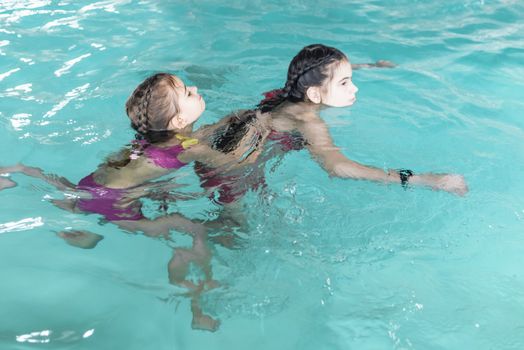 Two sisters in the pool. Two happy girls play in the pool.Beautiful girls swim and having fun in water.Active holiday.Two girls swim in the pool.