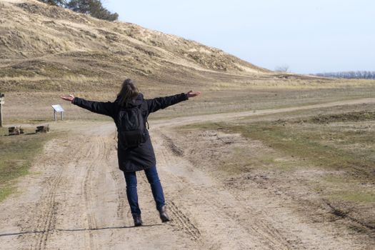 Caucasian woman in black coat arms raised on empty road towards sunset