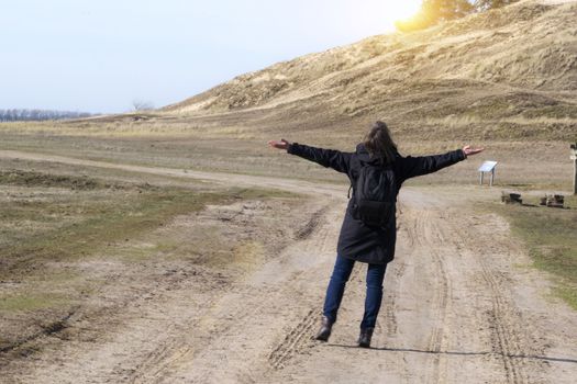 Caucasian woman in black coat arms raised on empty road towards sunset