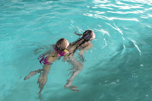 Two sisters in the pool. Two happy girls play in the pool.Beautiful girls swim and having fun in water.Active holiday.Two girls swim in the pool.