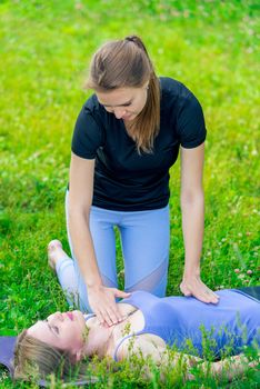 an experienced trainer controls the woman’s breathing during a yoga class in the park