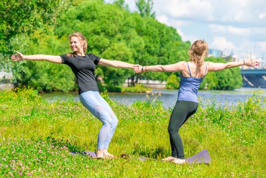 yoga trainer in class with a mature woman exercising in a summer park