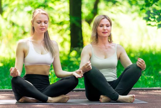 mature woman doing yoga in lotus pose with trainer individually in the park