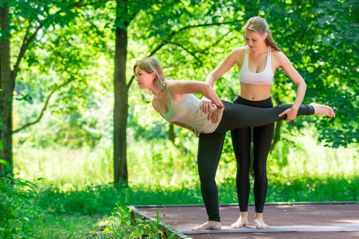 40 year old mature woman performs exercises with a trainer in a summer park.