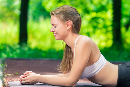 smiling slim woman playing sports in a summer park, portrait while doing an exercise