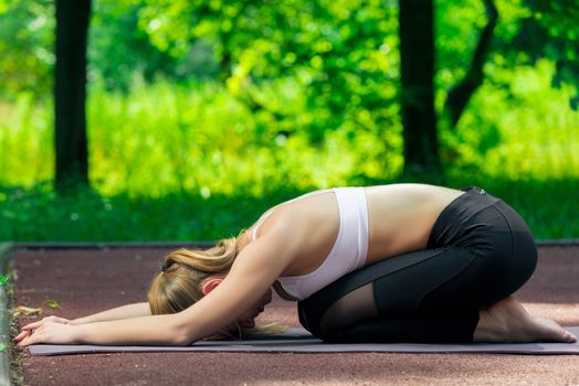 yoga on a mat in the park, portrait of an active slim trainer