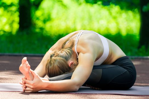 flexible pilates coach performs stretching exercises in the park on a sunny day