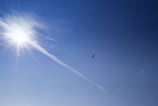Blue sky . Against the background of blue sky and bright sun, an airplane is flying. Basic background for design.Aircraft flying in the sky against a background of a bright sunset.