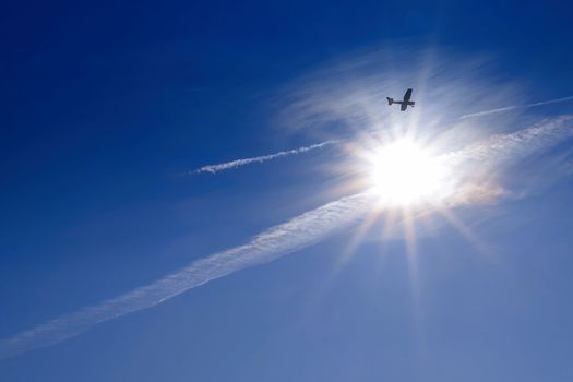 Blue sky . Against the background of blue sky and bright sun, an airplane is flying. Basic background for design.Aircraft flying in the sky against a background of a bright sunset.