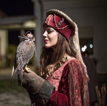 medieval woman holding a falcon on his arm. Lady looks at the hawk