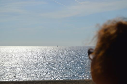 Beautiful silver path on the sea, curly head of a woman looking at the sailboats, rear view. Focus on the sea.