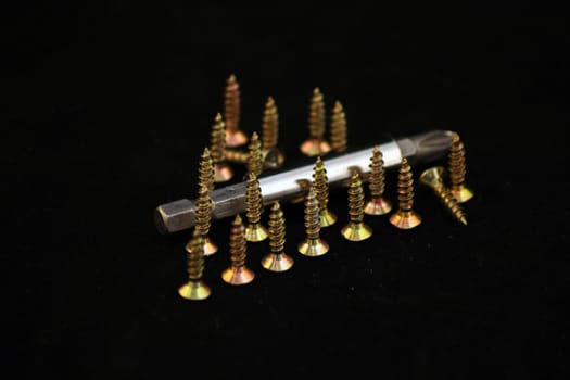 screws standing on hats in the shape of a triangle, and a nozzle for screwdriver on a black background.