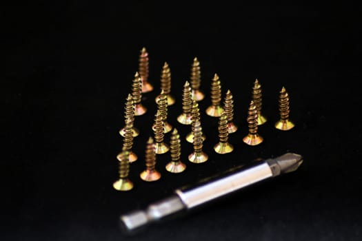 screws standing on hats in the shape of a triangle, and a nozzle for screwdriver on a black background.