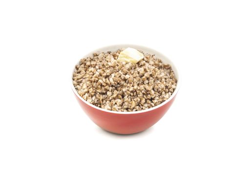 Dry buckwheat in red ceramic bowl with a piece of butter. Isolated on white background.