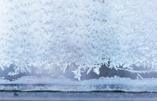 Winter beautiful crispy frost structure on a window with cold blue gradient light.