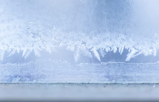 Winter beautiful crispy frost structure on a window with cold blue gradient light.