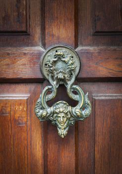 Antique bronze handle on wooden door. Decorative element. Close up.