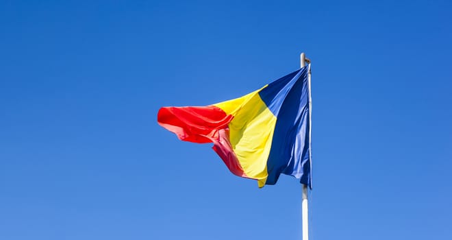 Romanian Flag on the mast. Romania flag of silk. Romanian flag on flagpole blowing in wind isolated against blue sky with copyspace.