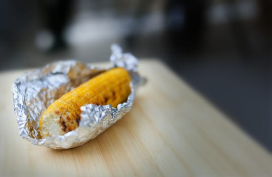 Baked yellow corn in foil on white wooden background