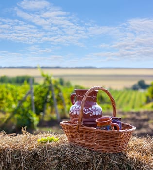 Concept of vine. Traditional Moldova story. Jug in basket of straw on background of the vineyards valley. Sunny day, blue sky
